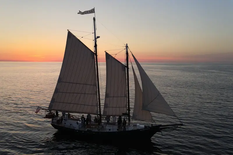 The schooner Serenity under sail at sunset, a golden horizon behind her