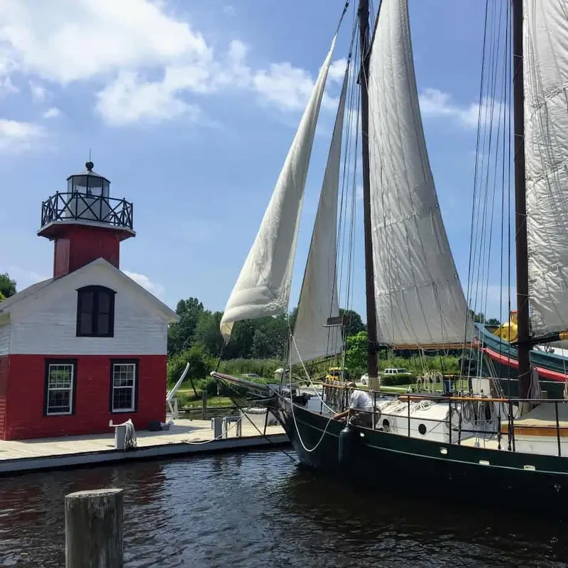 A two-masted schooner at a dock beside a small red lighthouse