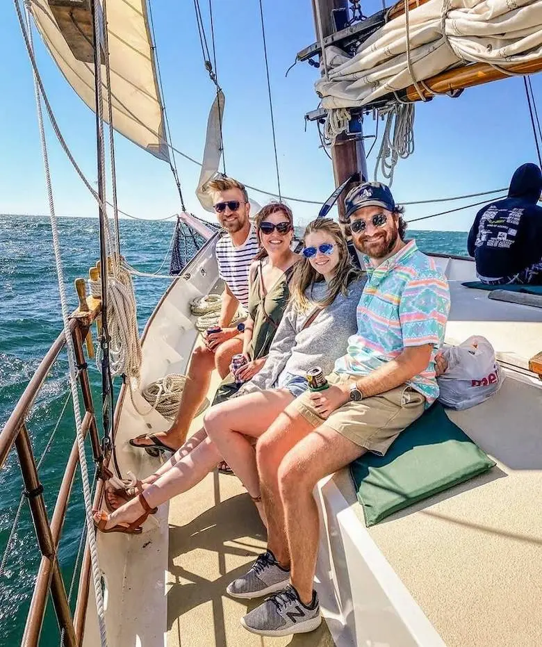 Four people smiling on the deck of a schooner, sails and rigging overhead